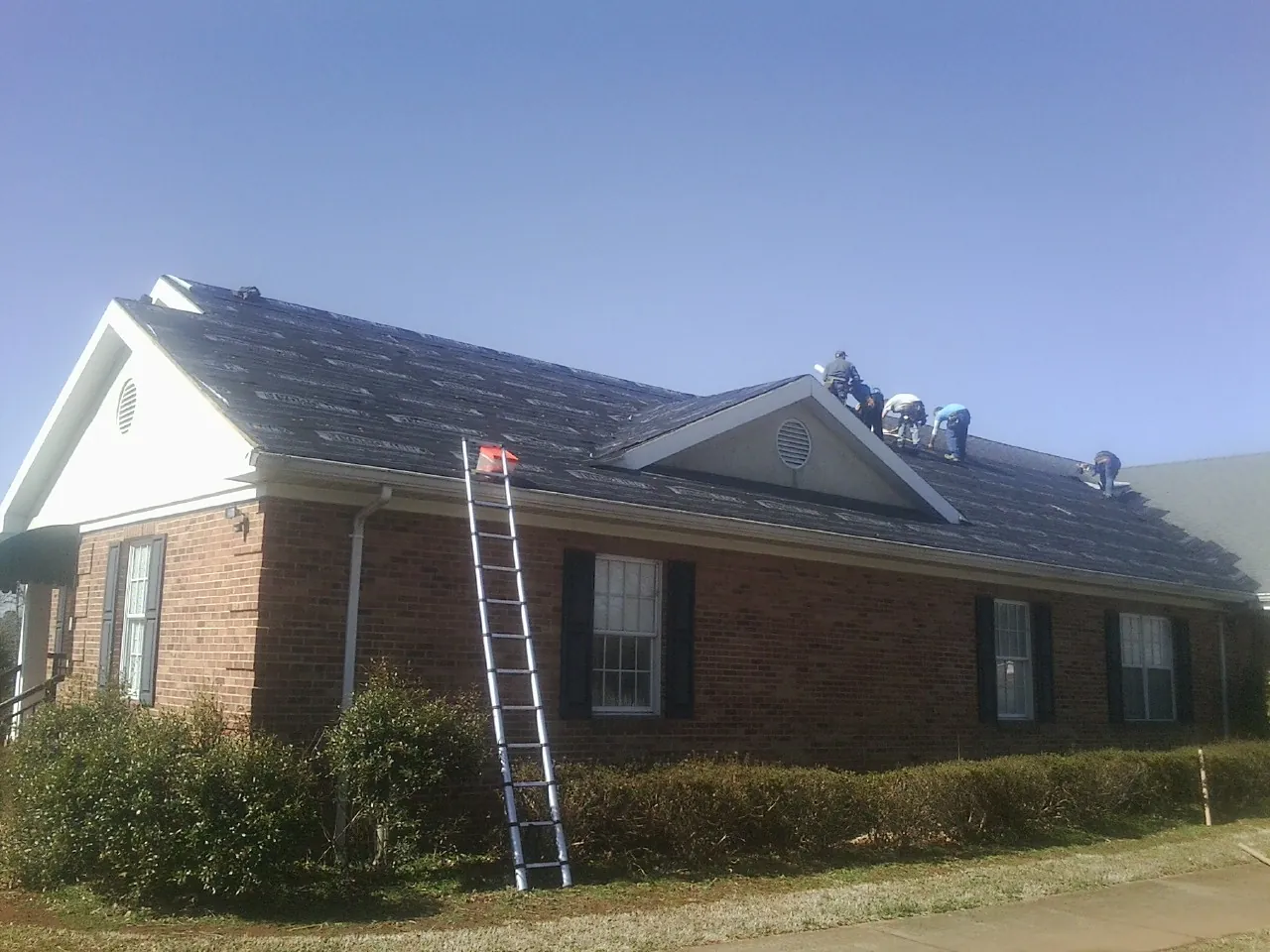 Crew tearing shingles off a brick ranch roof with a ladder set — Metal Roof Repair work by our crew in Peninsula