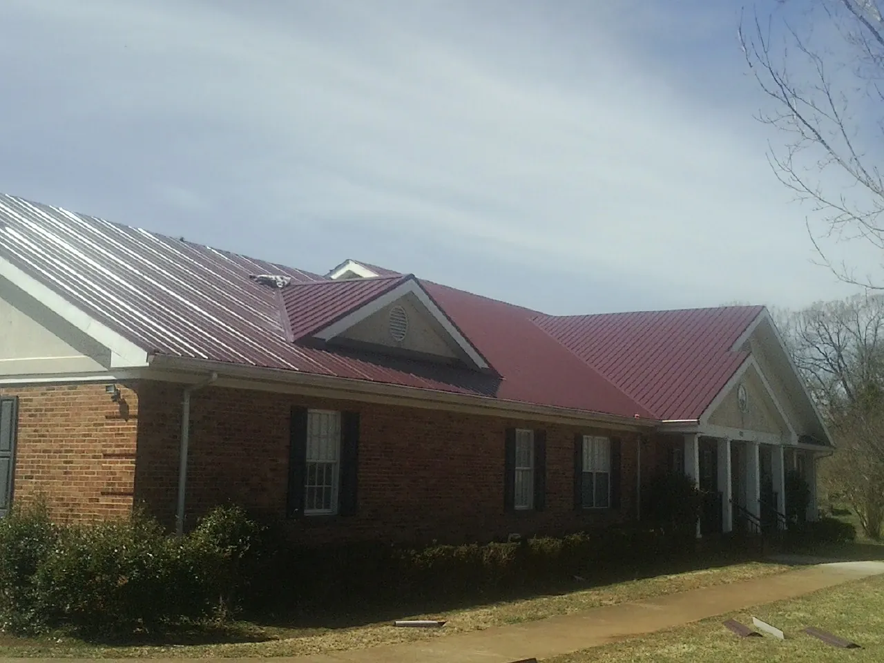 Red metal roof with gabled entries on a long brick building, from a Hail Damage Roof Repair job in Peninsula