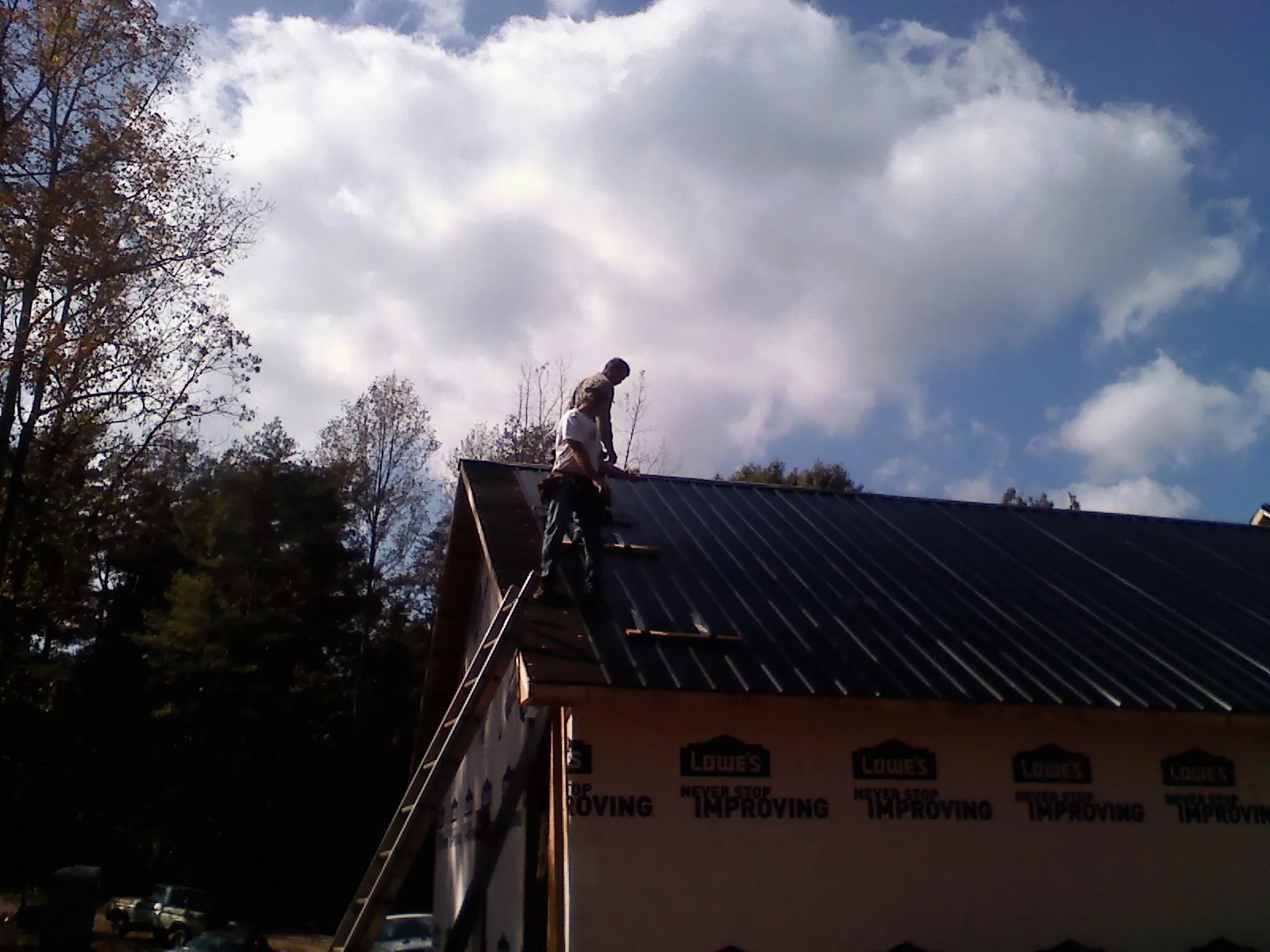 Roofer fastening dark metal panels high against a cloudy sky, from a Roof Inspection job in Peninsula